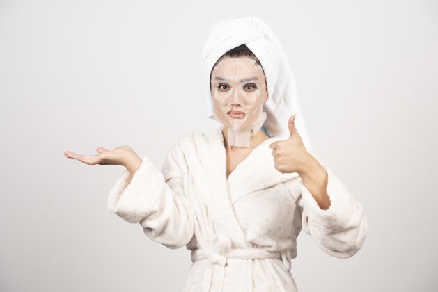 干净女人竖起大拇指 穿着浴衣和带面罩的毛巾成人漂亮肖像