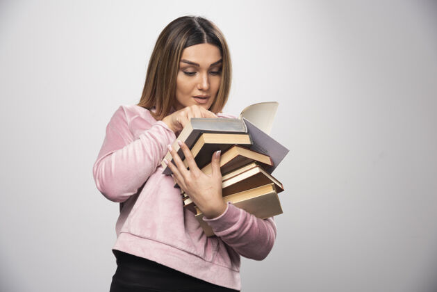 学习一个穿着粉色衬衫的女孩手里拿着一堆书 正试着用放大镜看上面的书呢小年轻人雇员