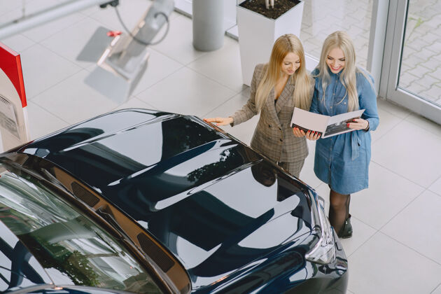 展示汽车沙龙里的女士买车的女士穿着蓝色裙子的优雅女士经理帮助客户汽车金发汽车