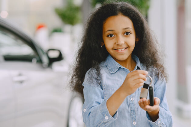 女孩快乐的 漂亮的小女孩 拿着车钥匙 展示它 微笑着摆姿势展厅交易车钥匙