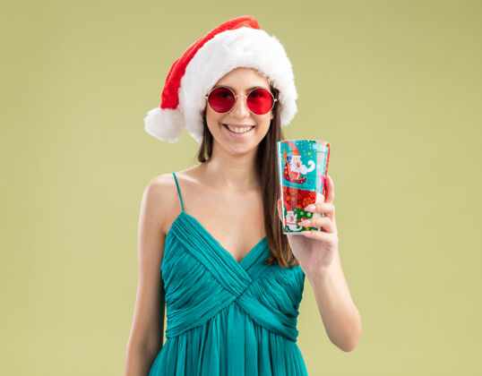 纸戴着太阳眼镜 戴着圣诞帽 手里拿着纸杯 面带微笑的白人女孩杯子绿色圣诞快乐