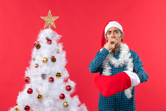 圣诞节一个戴着圣诞老人帽子 穿着蓝色条纹衬衫 展示圣诞袜子的年轻人大吃一惊惊喜圣诞树圣诞老人