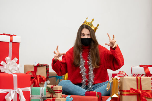 年轻女孩一个穿着红色毛衣的年轻女孩在礼物旁边摆着一副吓人的姿势 白色的面具上戴着黑色的面具脸红色礼物