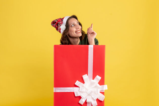 年轻站在黄色墙上盒子里的年轻女子的正视图购物礼物快乐