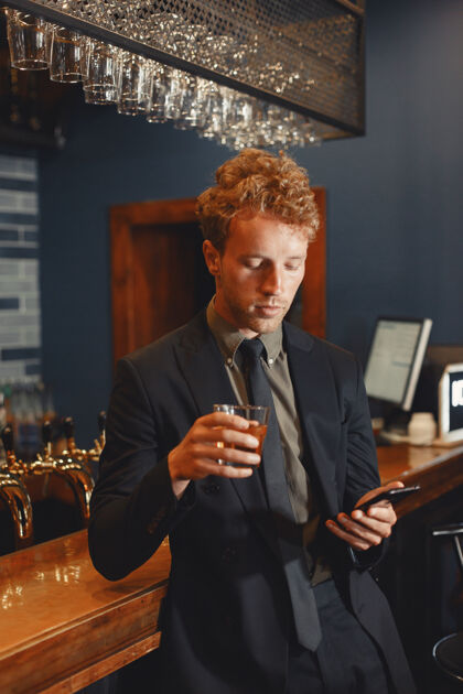 餐厅自信开朗的男人坐在吧台旁 喝着啤酒 用智能手机上网酒精啤酒喝酒