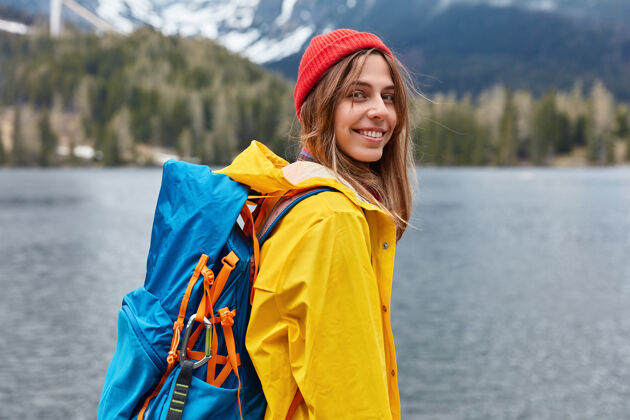 探险家快乐的欧洲年轻女子的后景享受着美好宁静的日子 大自然的风景 背着背包雨衣帽子高兴