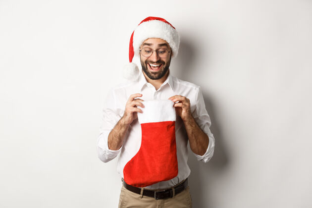 情绪化快乐的成年男子打开圣诞袜子 看看里面 收到圣诞礼物寒假 站在圣诞帽圣诞老人微笑冬天