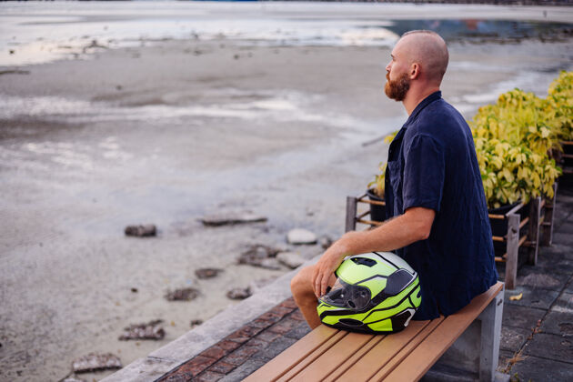 头盔日落时分坐在泰国长廊长凳上的戴着黄色头盔的男性摩托车手的画像自行车比赛户外