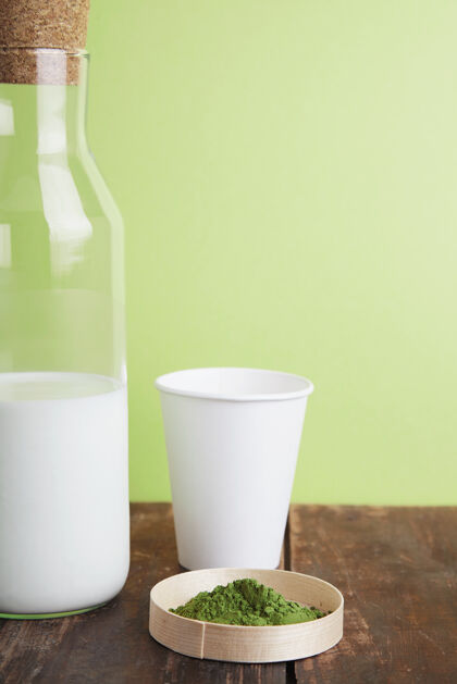 早餐古董奶瓶 白纸外卖玻璃和有机优质抹茶粉放在绿色简单背景前的棕色拉丝木桌上特写健康热木材