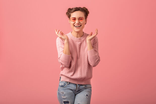 摆姿势穿着粉色毛衣 戴着墨镜 在粉色工作室的背景下 一个年轻漂亮的开怀大笑的女人女人笑开朗