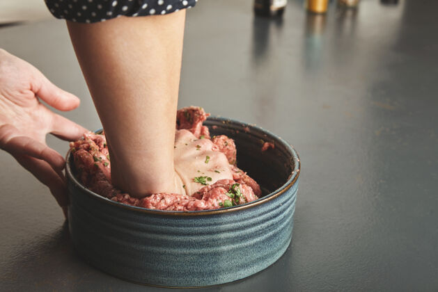 切碎的在蓝色的木桌上 女人们用手在陶瓷碗里揉肉末和香料牛肉带血的膳食