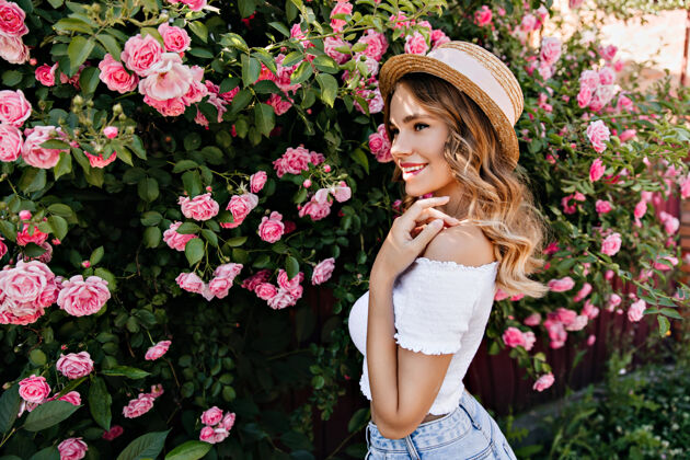 植物穿着白色背心的迷人女孩在美丽的花园里摆姿势戴着帽子的时尚女士享受玫瑰味道的户外镜头稻草乐趣可爱