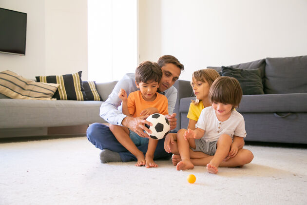 爸爸专注的爸爸拿着球和孩子们交谈可爱的白人爸爸和孩子们坐在客厅的地毯上一起玩耍童年 游戏活动和父亲的概念女儿孩子成人