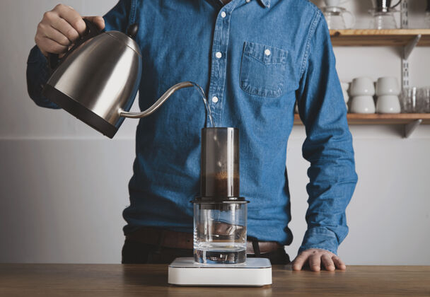 拿铁一步一步压榨咖啡身着蓝色牛仔裤衬衫的咖啡师将热开水从茶壶倒到aeropress专业咖啡冲泡咖啡店自动售货机分配器咖啡
