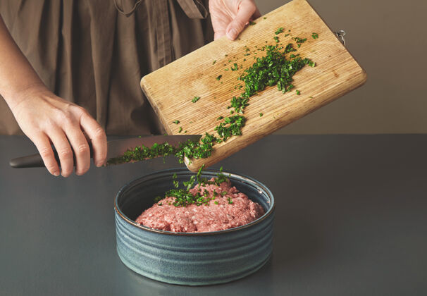 切碎的老木桌上漂亮的陶瓷碗里 女人用手在肉末中加入新鲜的绿欧芹配料堆香菜