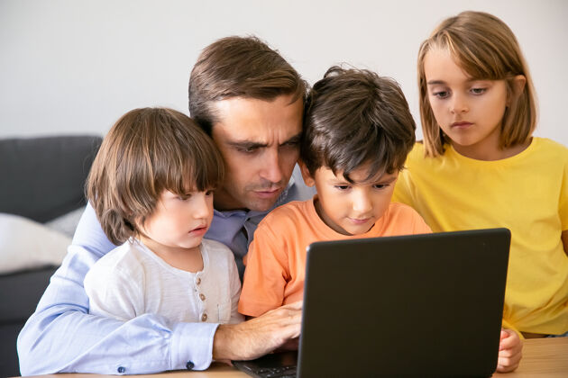 白种人专注的父亲和严肃的孩子看着屏幕白人中年父亲在笔记本电脑屏幕上打字 孩子们在看他的工作父亲 童年和数字技术的概念父亲童年打字