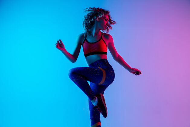 运动年轻漂亮的女人穿着鲜艳的运动服 在霓虹灯下以渐变的粉蓝色为背景图形年轻运动