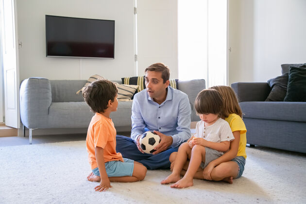 儿子高加索爸爸抱着球和孩子们聊天可爱的中年爸爸和孩子们坐在客厅的地板上一起玩耍童年 游戏活动和父亲的理念可爱可爱朋友