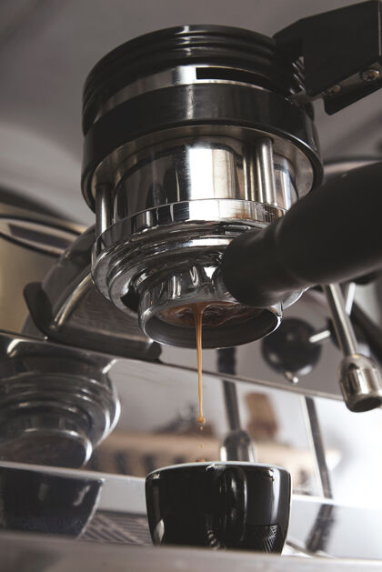 咖啡师特写镜头：从银色金属咖啡机倒进黑色陶瓷杯中的浓缩咖啡专业咖啡酿造从顶部滴下几滴烤咖啡分配器倒酒饮料