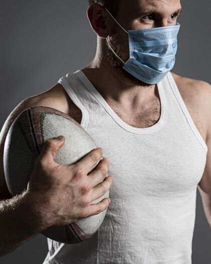 垂直戴着医用面罩拿着球的男性橄榄球运动员的前视图锦标赛比赛体育