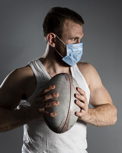 完全接触戴着医用面罩手持球的男性橄榄球运动员的前视图体育比赛球