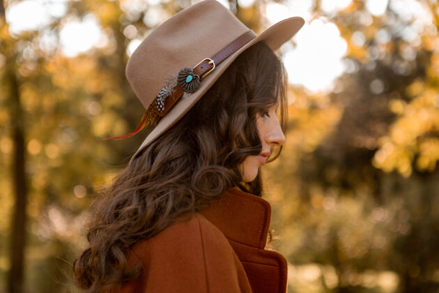 波西米亚画中有魅力的时尚女人留着长长的卷发漫步在公园里穿着温暖的棕色外套秋日时髦 街头风格戴着帽子连衣裙姿势配饰