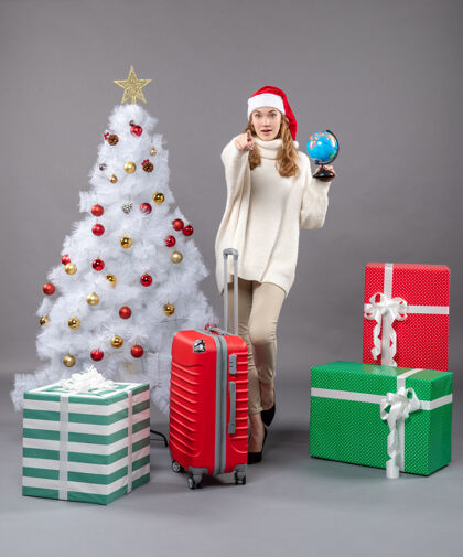 礼物正面图：戴着圣诞帽的金发女孩拿着红色手提箱附近的地球仪圣诞盒子礼品盒