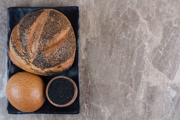 视图黑芝麻面包和一小碗黑芝麻放在大理石盘上种子酥皮外壳