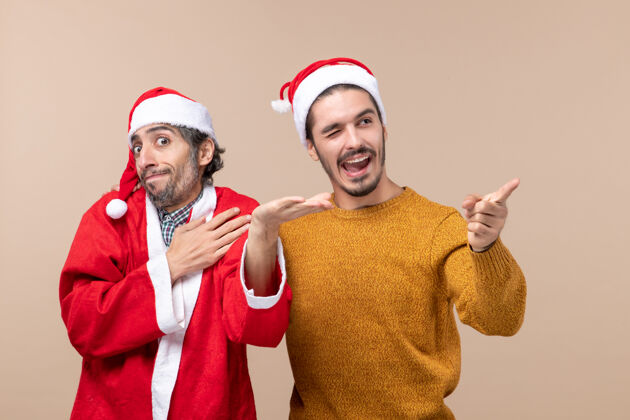站立正面图两个圣诞老人戴着圣诞帽站在米色孤立的背景上服装视图帽子