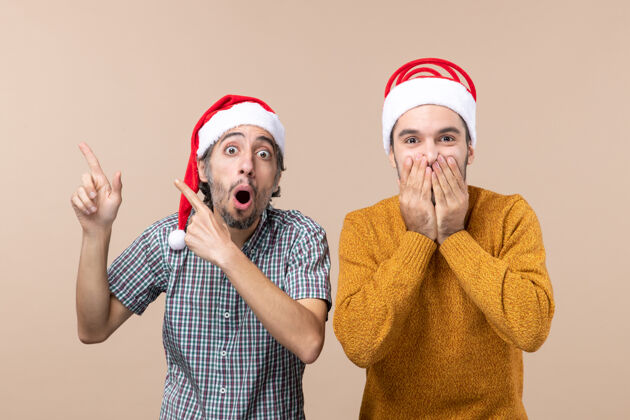封面正面图两个戴着圣诞帽的男人 一个在展示什么 另一个在米色背景下用手捂住脸前面展示脸
