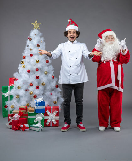 人们圣诞老人和男厨师在灰色墙上围着圣诞礼物的正视图圣诞庆祝厨师