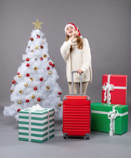 东西正面图惊异的女孩拿着旅行箱 展示着什么圣诞帽时尚快乐