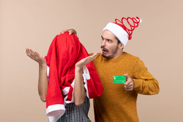 圣诞老人正面图两个朋友 一个拿着信用卡 一边摸他的头 另一个用圣诞老人的外套盖着他的头 背景是米色的视图米色朋友