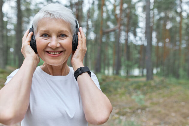 老年照片中的中年妇女手拿耳机 一边在户外慢跑一边听音乐训练护理运动装