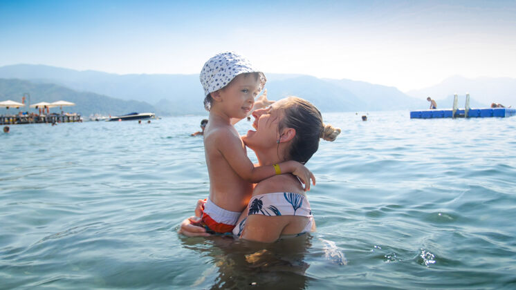 海洋快乐欢笑的男孩和妈妈在海里玩耍的画像反思拥抱欢呼