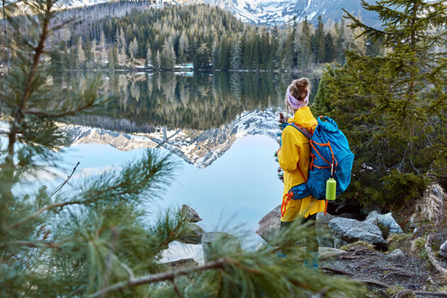 湖泊带着包的年轻旅行者的户外镜头 背对着镜头 欣赏山峦 新鲜空气和小湖徒步旅行木头背包