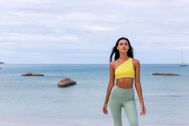 锻炼海滩上穿着五颜六色运动服的迷人年轻女子人健康健身