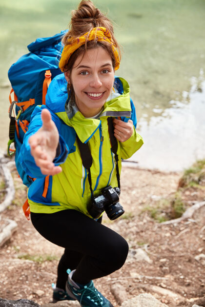 向上给我一个满意的女性度假者试图爬山的垂直镜头 在绿松石湖附近摆姿势 在镜头里伸出手垂直风景海岸