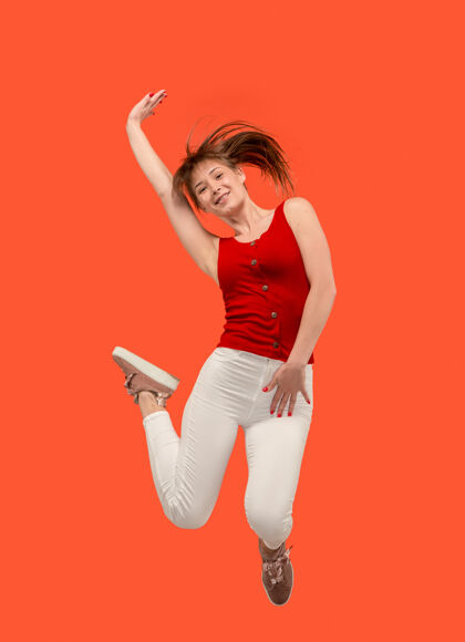 无忧无虑移动中的自由在橙色工作室背景下 美丽快乐的年轻女子跳跃和做手势的半空中镜头在运动中奔跑的女孩人类情感和面部表情的概念舞蹈年轻表情