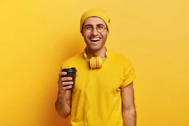牙齿帅气开朗的男人用耳机捧着外卖咖啡 心情很好高兴美味衣服