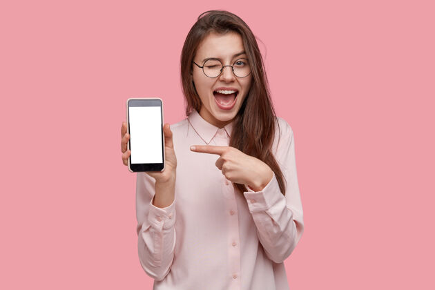 手机看着这部手机开心快乐的女人眨着眼睛 用食指指着空白的屏幕 显示出现代的装置电子眼镜显示器