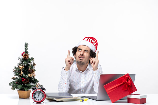 商人困惑的年轻商人 戴着滑稽的圣诞老人帽 在白色背景的办公室里往上看 想着什么办公室电脑困惑