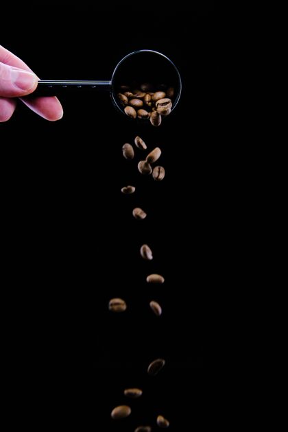 木头垂直拍摄的一个人的手倒咖啡豆从勺子在黑色浇注垂直芳香