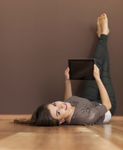 向上快乐的女人躺在地板上用数字平板电脑牙关脚垫连接