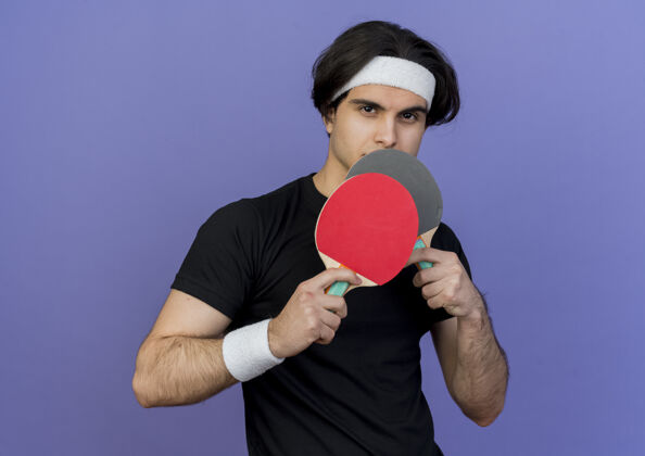 严肃穿着运动服 头戴头巾 手拿球拍打乒乓球的年轻人 表情严肃蓝色网球看着