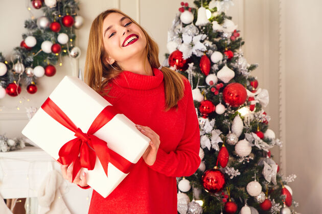 青少年微笑的女人拿着许多礼品盒在装饰好的圣诞树旁摆姿势圣诞快乐友好人们