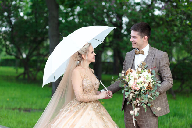 庆祝快乐的新郎新娘打着白色雨伞 在夏天的公园里露天婚礼未婚夫大学学生