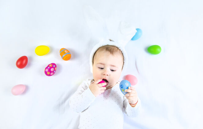 肖像宝宝穿得像兔子 在白色的表面上放复活节彩蛋复活节表情婴儿