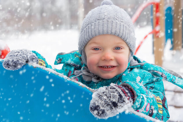 衣服冬天 一个穿着暖和的连体衣的小男孩在外面的操场上玩耍男孩冬天雪