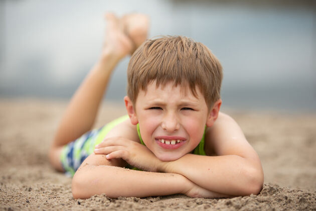 天真一个小学生躺在沙滩上孩子在夏天的水边海岸男人脸金发